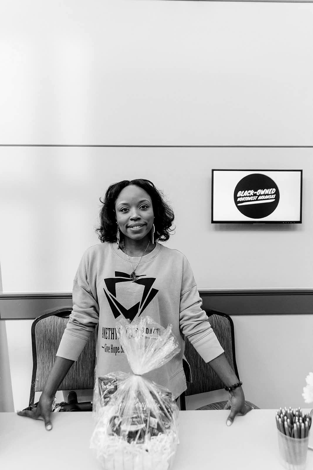 A smiling vendor standing at her Expo table in front of a Black-Owned NWA sign